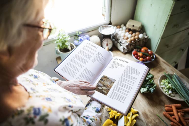 Happy elderly woman reading a cookbook